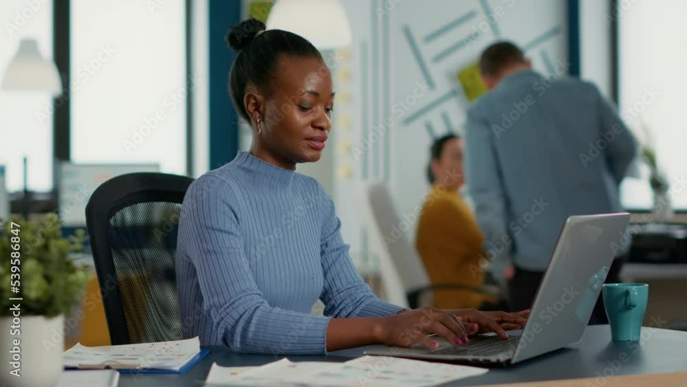 Poster portrait of african american woman typing using laptop keyboard and smiling at camera sitting at des