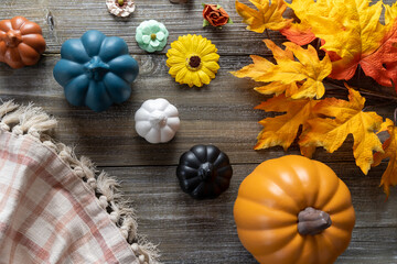 Colorful fall flatlay, top-down view of fake pumpkins, plaid towels, and maple leaves on a wood background