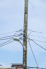 Jumble of wires connecting to the top of a wooden telephone utility pole with a street light...