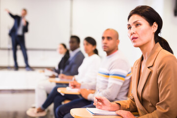 Focused asian businesswoman sitting with colleagues in conference room during corporate seminar