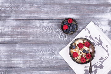 Homemade granola with nuts, raspberries and blueberries on a gray whitewashed rustic table, top view, copy space. Healthy breakfast