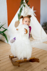 Little african american girl riding plush white rocking llama at home