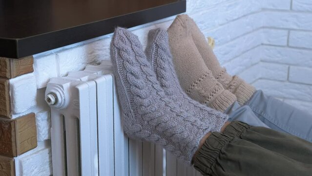 Friendly children in woolen socks. Two friendly children legs in woolen knitted legs get warm on home radiator during cold winter day.