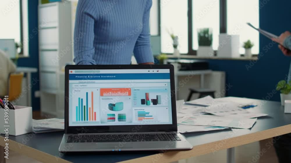 Poster closeup of laptop screen showing moving charts and financial statistics on desk in busy startup offi