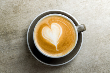 Cappuccino coffee with heart drawing on grey table top view