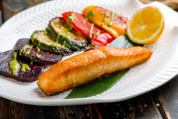 Salmon steak on the grill with grilled vegetables on white plate macro close up