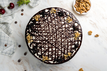 cake with prunes and walnuts poured with chocolate on white marble table top view