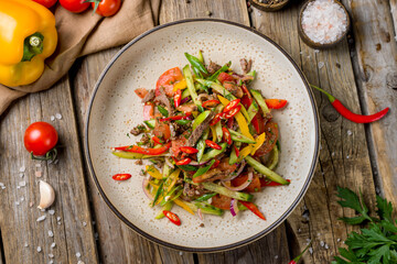 asian salad with beef, vegetables and spicy pepper on blue uzbek plate top view on old wooden table