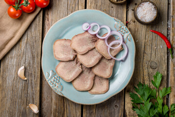 Beef tongue with red onion rings on old wooden table top view