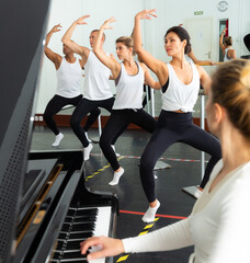 Ballet students doing exercises near barre with musician at piano