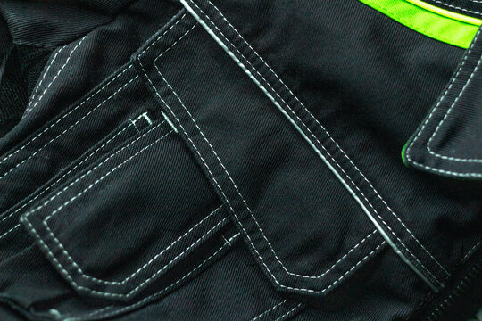 White stitching on black fabric. Texture of black working clothes white stitching closeup, green reflective elements
