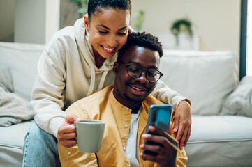 Multiracial couple at home while drinking coffee and using smartphone