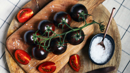 Black tomatoes on a branch on a wooden board with sea salt.