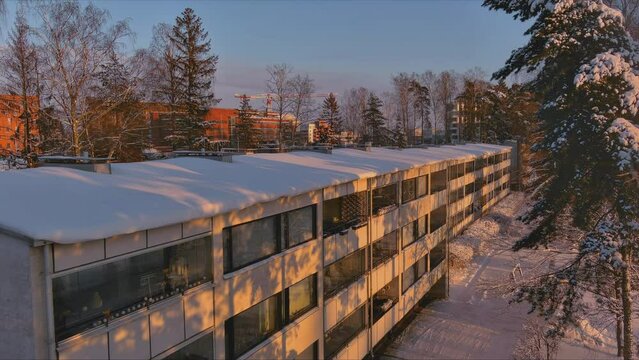 Espoo.Finland-February 3.2022: Aerial shot of a snow covered building in Keilaranta in Espoo Finland. Trees. Snowy city. Residential area. Nordic winter. Drone slowly moving upwards.