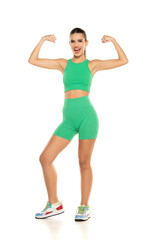 young sporty smiling woman in green shorts and top showing biceps on white background
