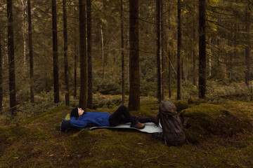 A caucasian man with a backpack lying down resting in forest.