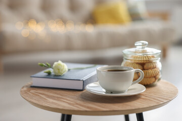 Cup of coffee, cookies, book and eustoma flower on wooden table in living room