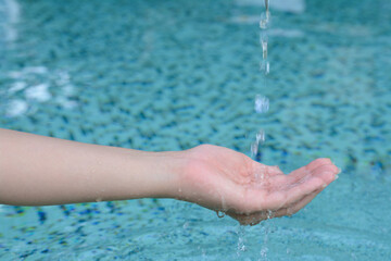 Water pouring into the girl's hand above pool, closeup