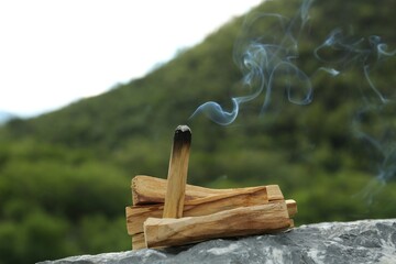 Burning palo santo stick on stone surface outdoors, closeup