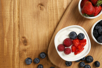 Yogurt served with berries on wooden table, top view. Space for text