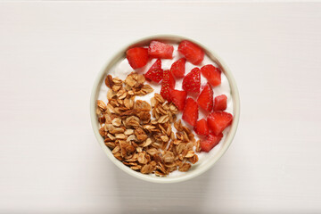Yogurt served with granola and strawberries on white wooden table, top view