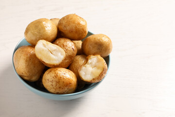 Bowl of tasty whole baked potatoes on white table, space for text