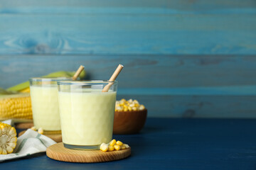 Tasty fresh corn milk in glasses and cobs on blue wooden table. Space for text
