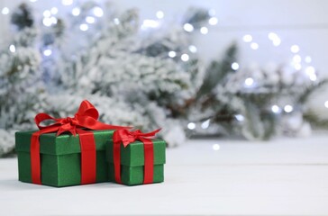 Beautiful gift boxes on white table against blurred festive lights, space for text. Christmas present