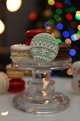 Beautifully decorated Christmas macarons on white table against blurred festive lights