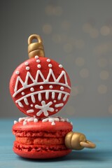 Beautifully decorated Christmas macarons on light blue wooden table against blurred festive lights, closeup