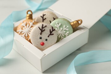 Beautifully decorated Christmas macarons in box and ribbon on white table, closeup