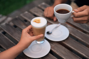Man and woman drinking coffee at wooden table in outdoor cafe, closeup