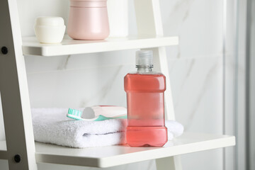 Fototapeta na wymiar Bottle of mouthwash, toothpaste and brush on white shelf indoors
