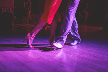 Dancing shoes of a couple, couples dancing traditional latin argentinian dance milonga in the ballroom, tango salsa bachata kizomba lesson, festival on a wooden floor, purple, red and violet lights