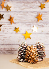 Naklejka na ściany i meble Christmas and New Year decoration with pine cones, golden shinning stars, light wooden background, copy space