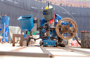 A welder is welding the bottom plate of a large oil tank with an automatic welding machine.