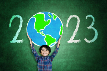 Little boy lifting a globe drawn with 2023 number