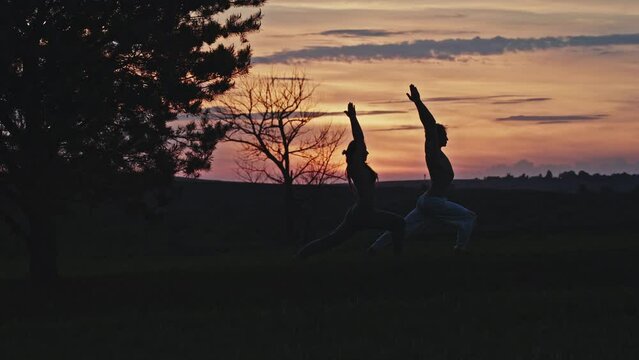 Couple Practices Yoga Moving In Sync Against Purple Sunset