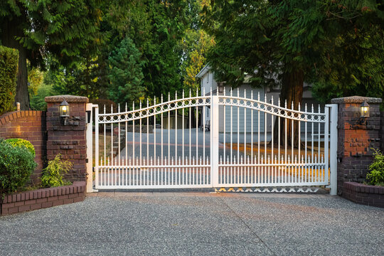 Iron front gate of a luxury home. Wrought iron white gate and brick pillar.