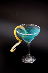 Blue Curacao liqueur in a tall glass with lemon zest and sugar on a black background.