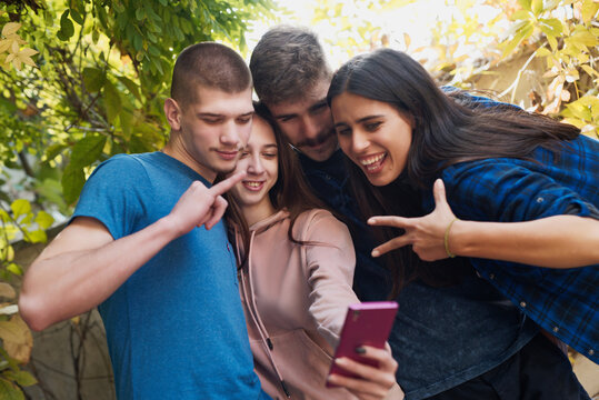 Group of four young teen friends taking a selfie, using her friend's phone to take a picture