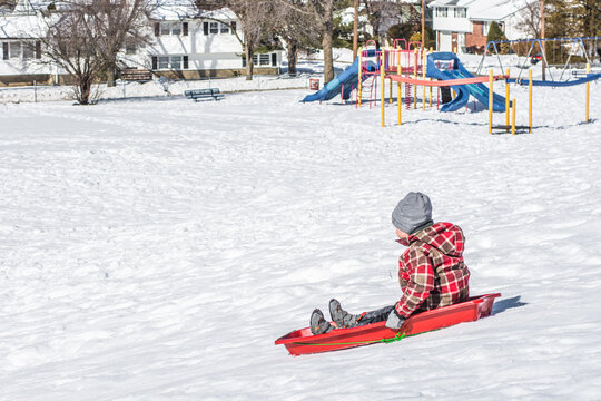 The boy slides from the snowy hill on a sled.