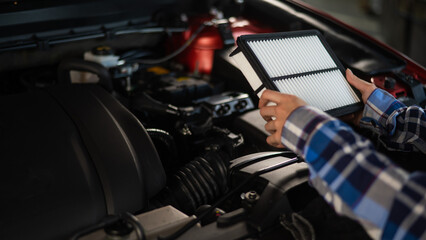 Caucasian female auto mechanic changes the engine air filter in the car.