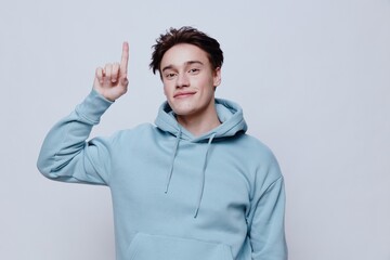Fototapeta premium horizontal portrait of a pleasantly smiling young man in a light hoodie pointing his fingers towards an empty space on the background
