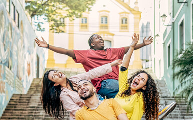 Group of happy young multiracial friends with arms raised up having fun in the city street - Friendship and travel concept - Focus on the bearded man.