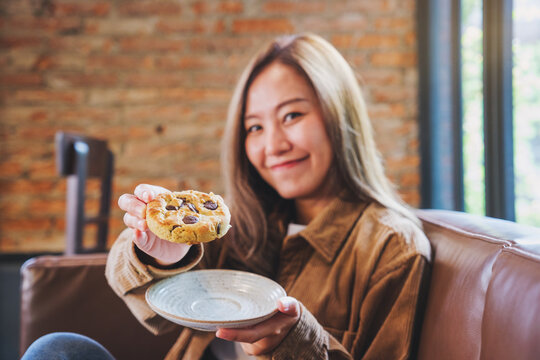 Portrait image of a beautiful young asian woman holding and showing a piece of cookie