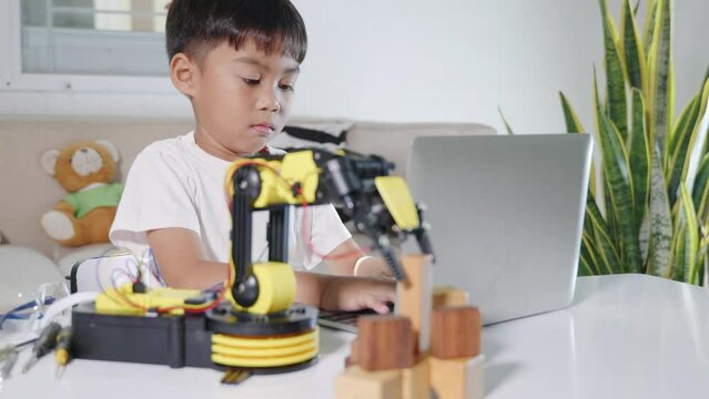 Asian little kid boy using laptop computer check on robotic arm machine in workshop, Child learning lesson programer to programming control robot arm pick up wood block, Technology science education