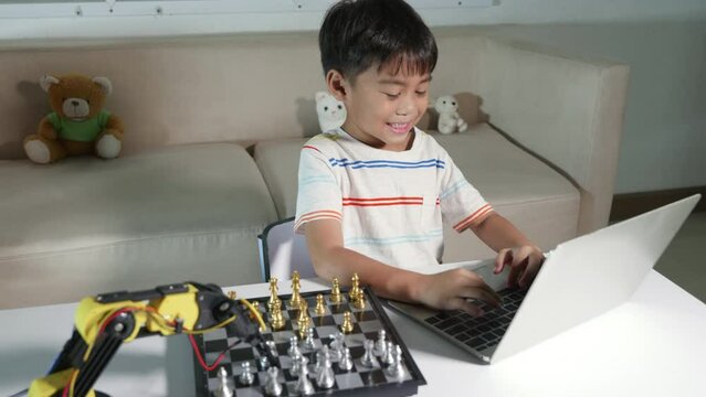 Asian little boy programming code to robot machine arm on laptop for play chess, STEM education E-learning, Funny children learning getting lesson control robot arm, Technology science education
