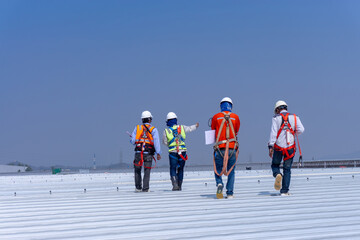 Team engineers wearing full safety body harness working on roof top for inspection metal roof sheet...