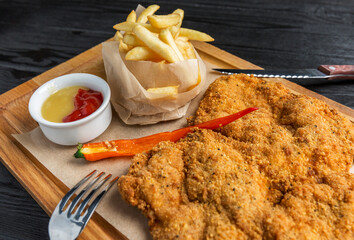 Appetizing breaded fried schnitzel and french fries with sauce. The dish is served on a wooden...